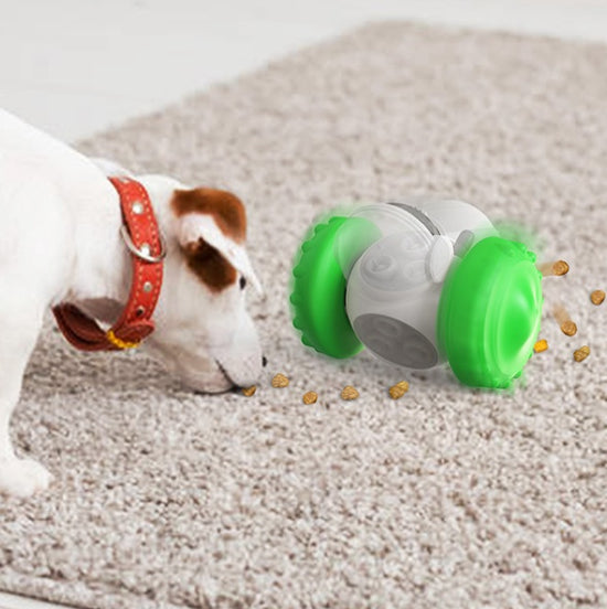 Interactive pet treat dispenser toy with a spinning, tumbler design, featuring a white body, green textured wheels for grip, and a clear compartment showing treats. Inset shows a cat and dog interacting with similar toys